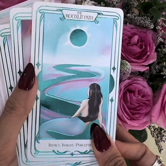 Tarot card titled 'The Moonlit Path' held by a hand with pink roses in the background